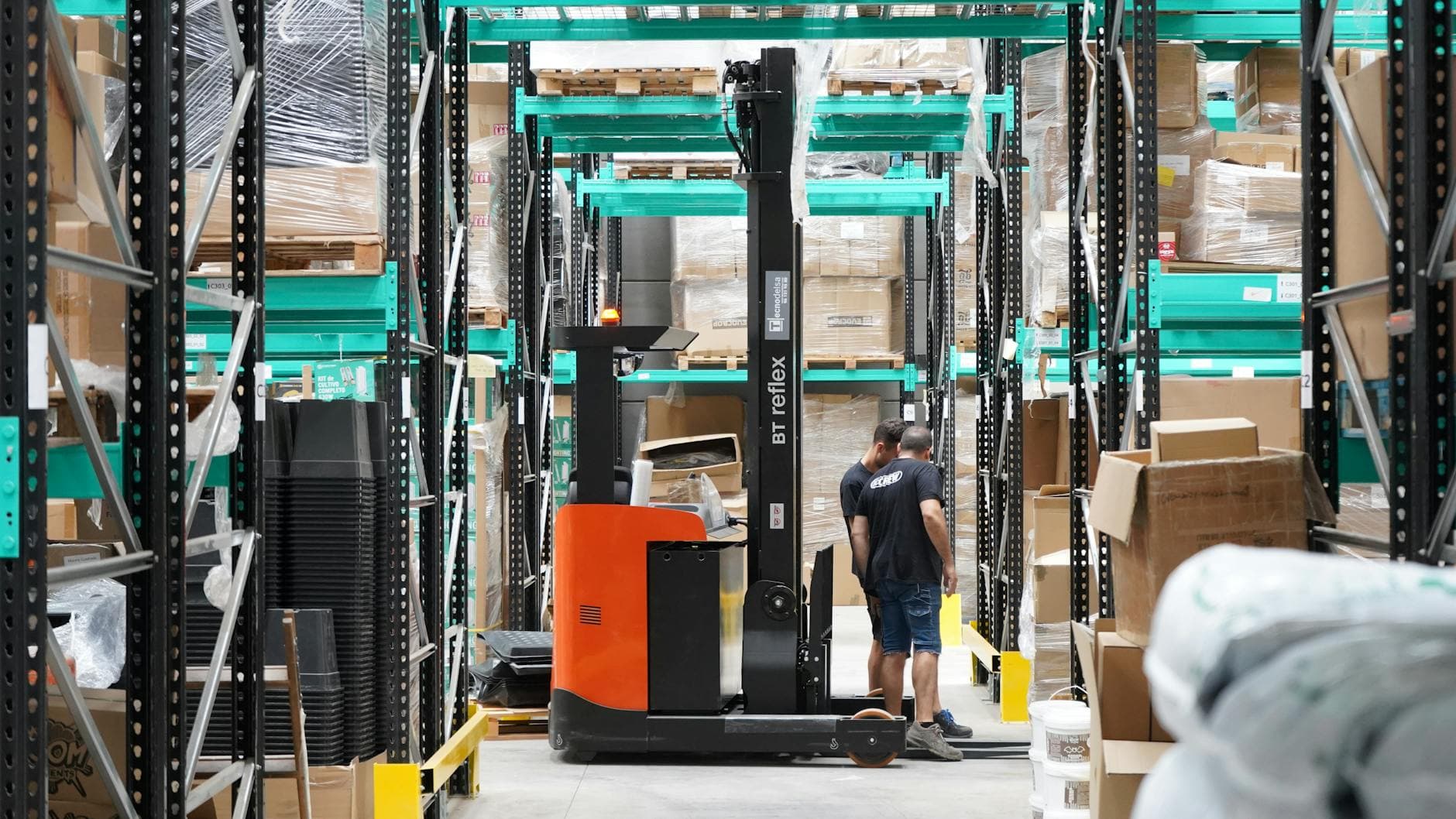 Warehouse scene featuring workers and a forklift navigating aisles for logistics and inventory management.