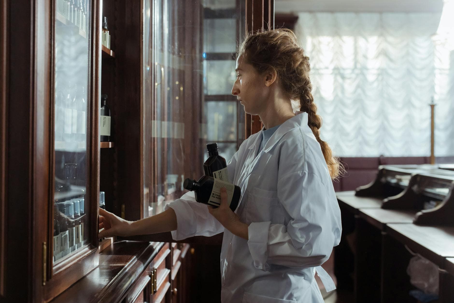 A female pharmacist arranging bottles in a classic pharmacy interior, captured indoors.